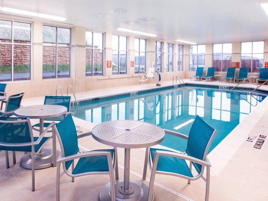 An indoor swimming pool with clear blue water, surrounded by blue chairs and tables.