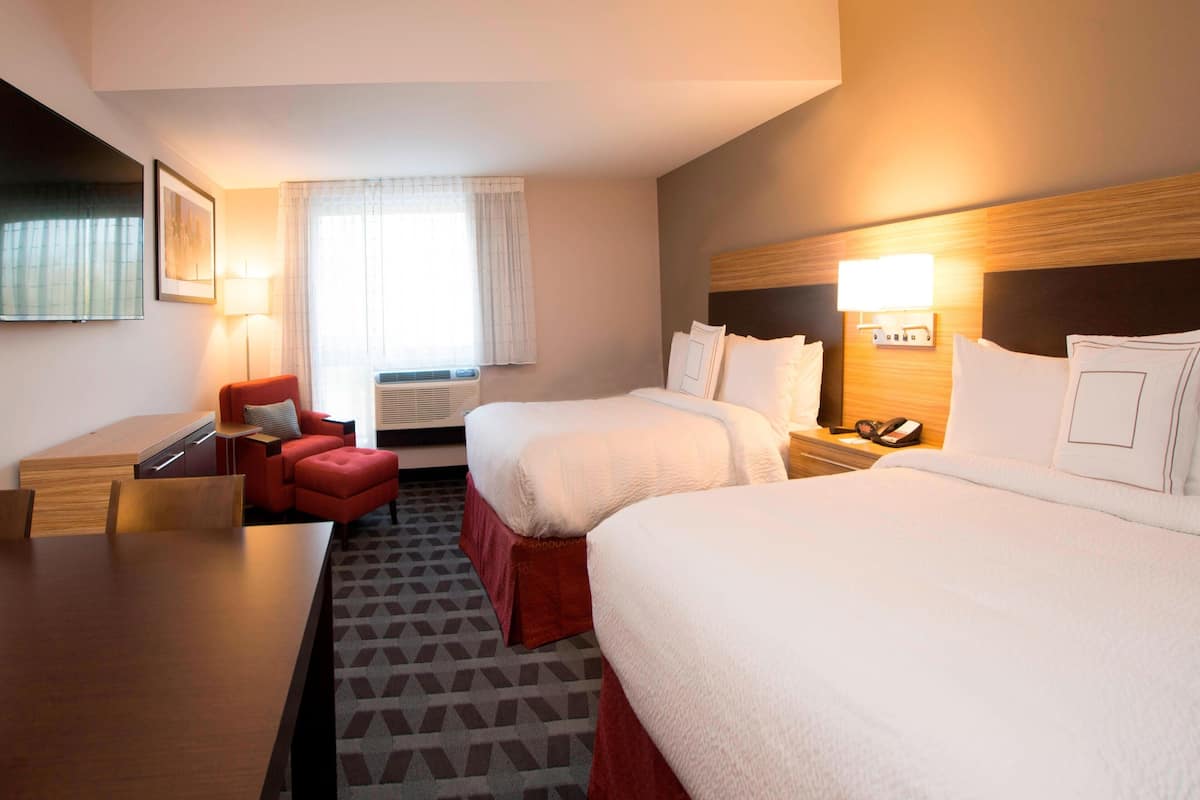 A hotel room with two beds, a desk, a chair, and a lamp.