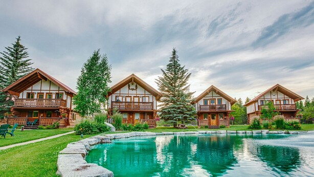 A row of log cabins with balconies, a swimming pool, and a well-maintained lawn.