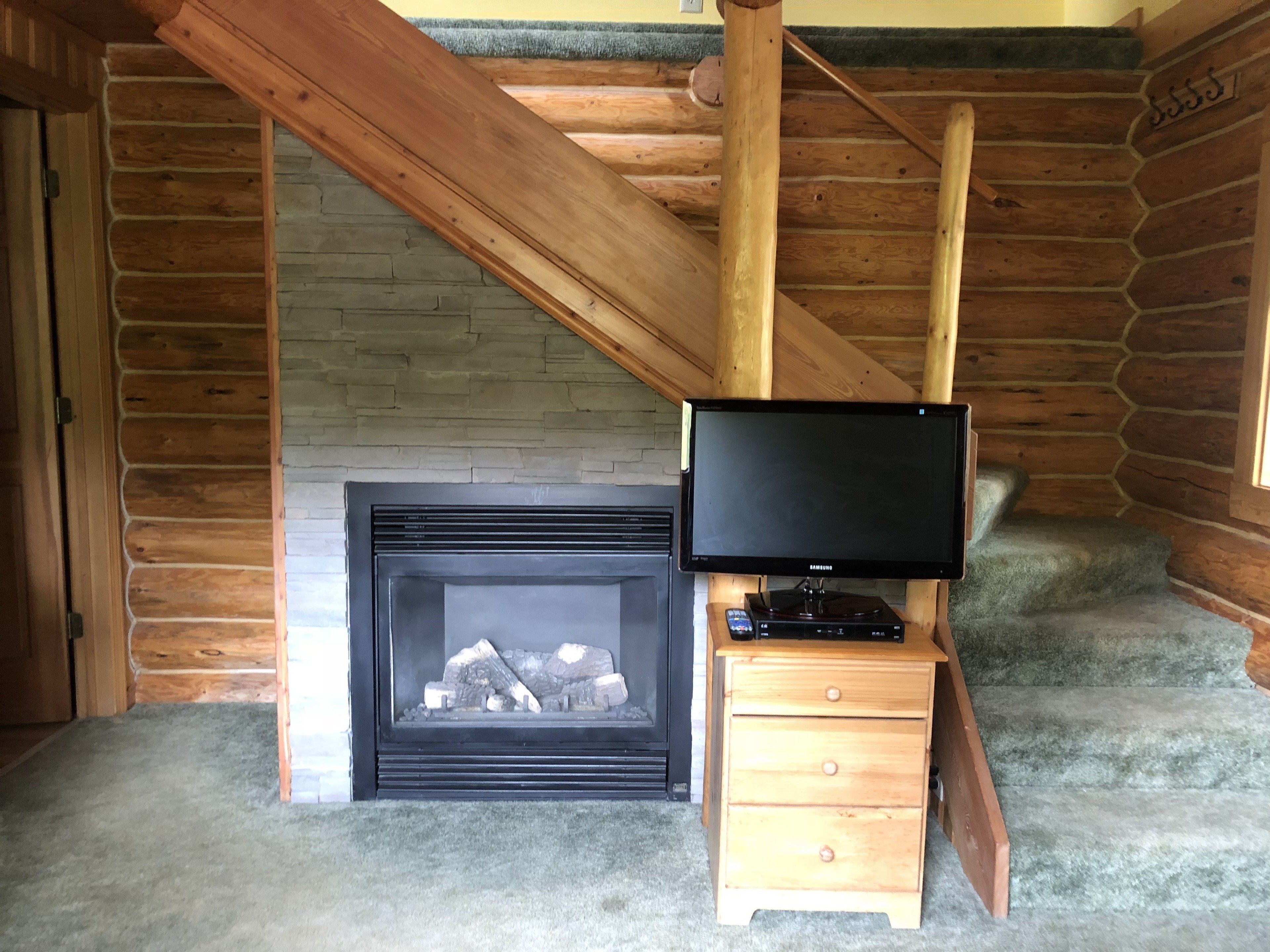 Ein rustikales Blockhaus-Interieur mit Kamin, Fernseher auf einem Holzboden und einer Treppe.
