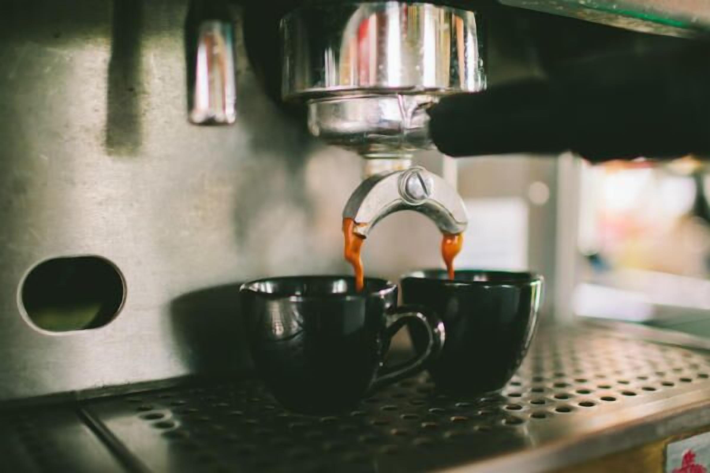 Une machine à café distribue de l’expresso dans deux tasses noires.