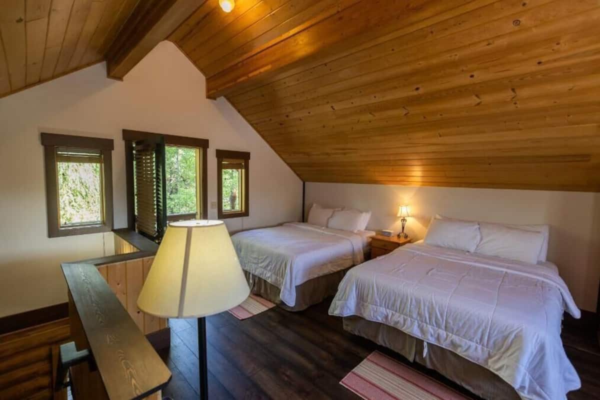 A bedroom with two beds, a wooden ceiling, and a desk with a lamp.