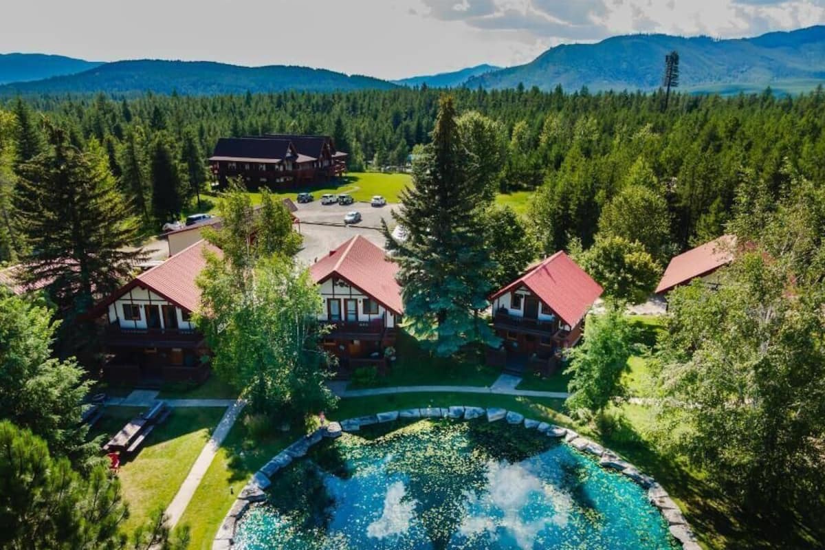 A lodge with multiple red-roofed cabins, a swimming pool, and a forested backdrop.