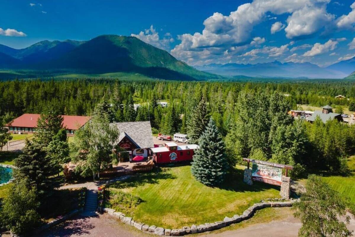 A lodge with a red building, surrounded by dense forest and mountains.