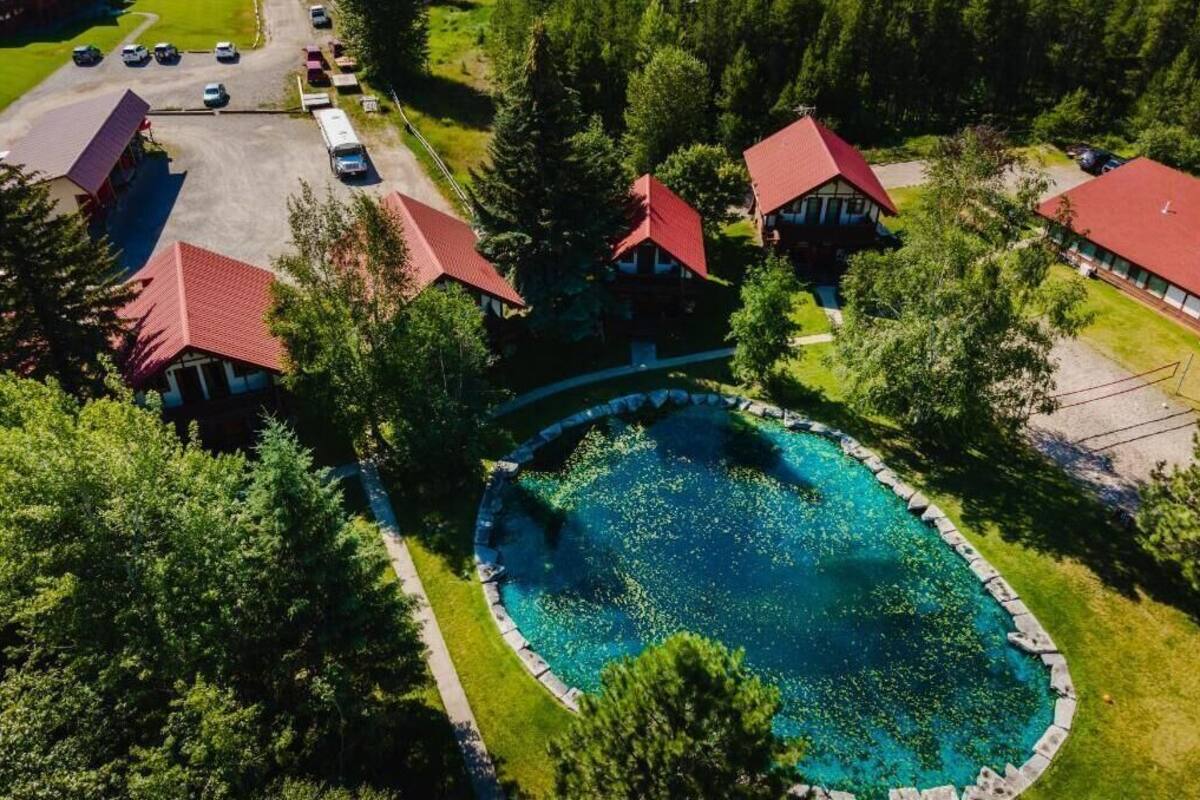 An aerial view of a resort with a central swimming pool surrounded by buildings with red roofs, surrounded by dense greenery.