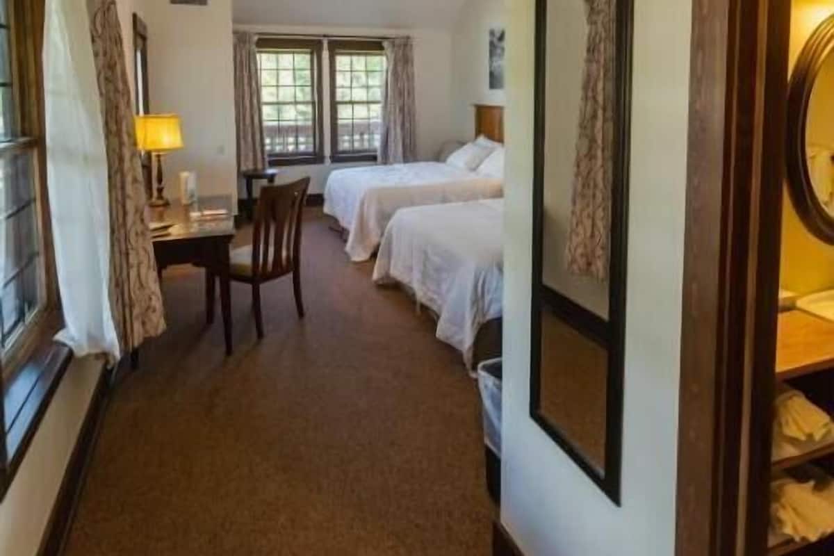 A hotel room with two beds, a desk, a chair, a ceiling fan, and a framed picture on the wall.