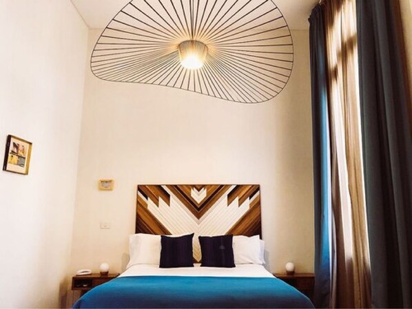 A hotel room with a bed, a modern ceiling light fixture, and a nightstand.
