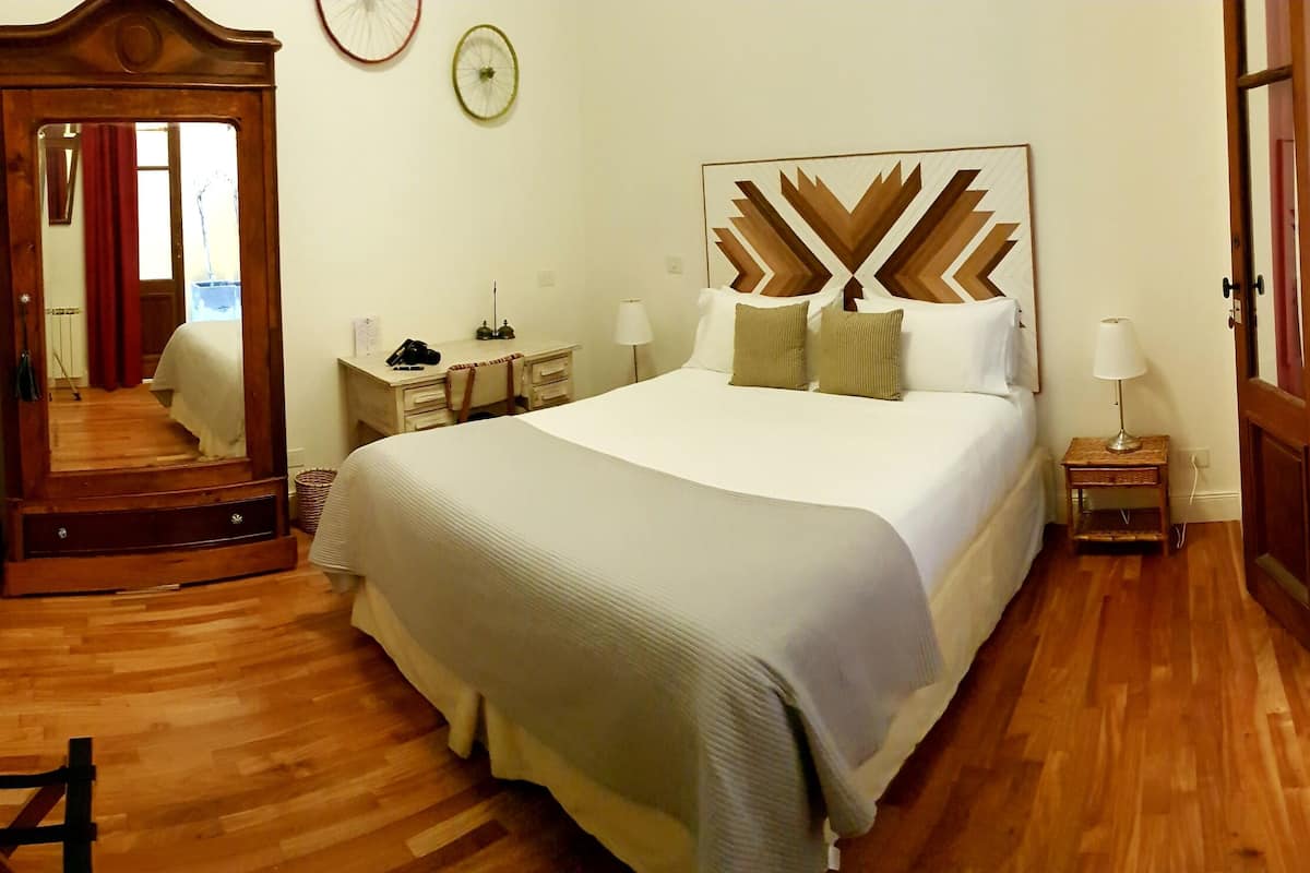 A hotel room with a large bed, a wooden desk, a chair, a mirror, and a wardrobe.