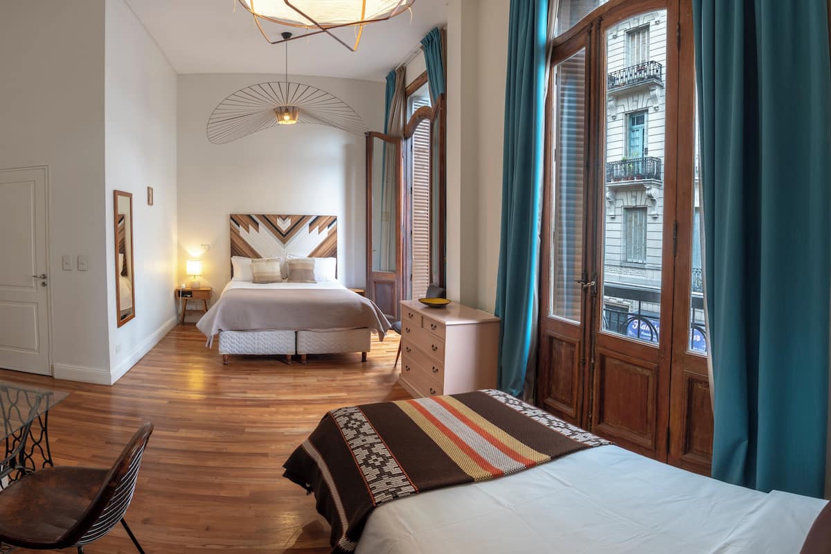 A bedroom with a large bed, a desk, a chair, and a window with curtains.