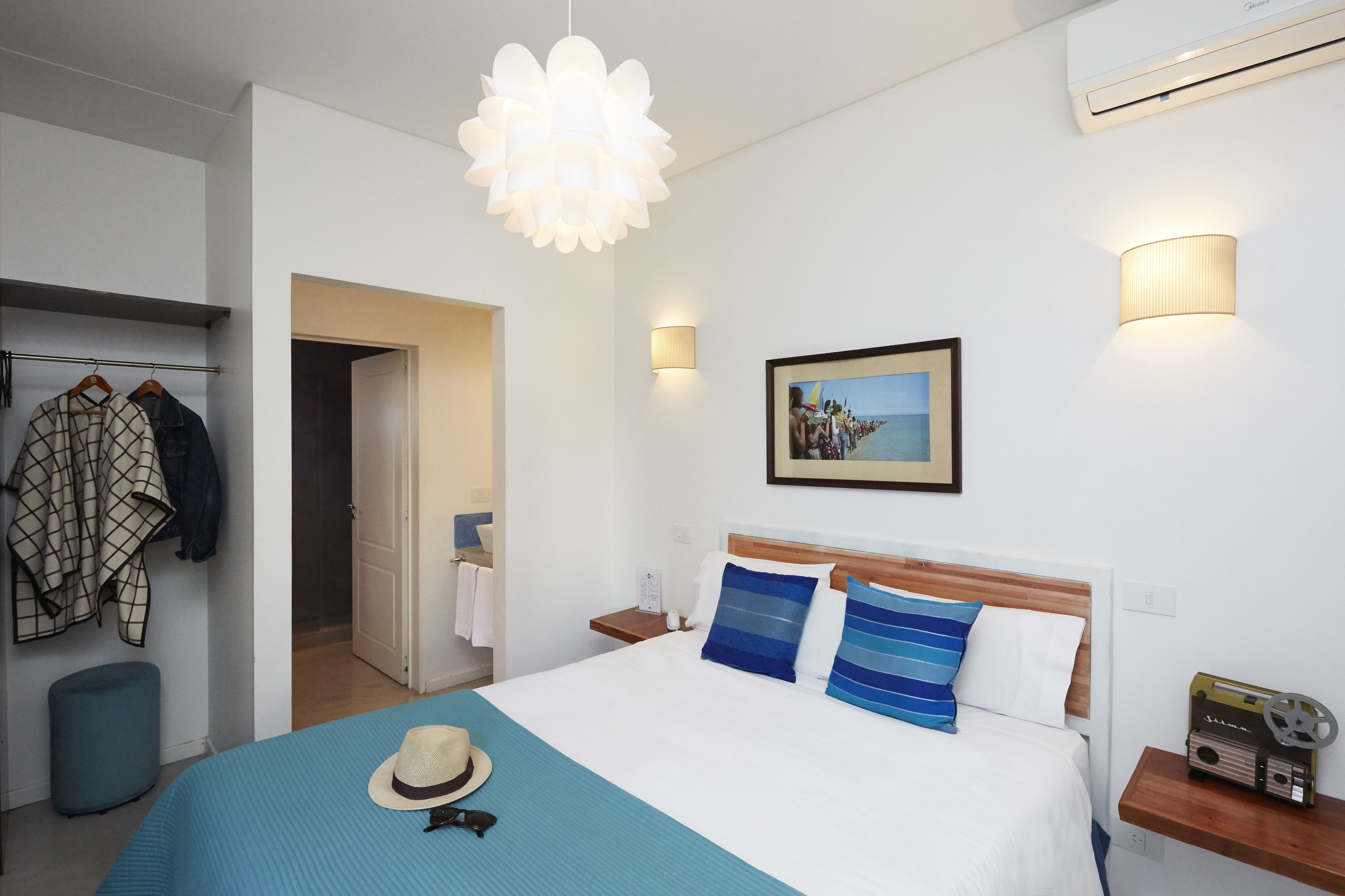 A hotel room with a bed, a wardrobe, a hanging light fixture, a wall-mounted picture, and a bedside table with a radio.