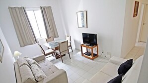 A living room with a sofa, a dining table with chairs, a TV on a stand, and a window with curtains. - Rio Spot Apartments D026 (Rio de Janeiro)