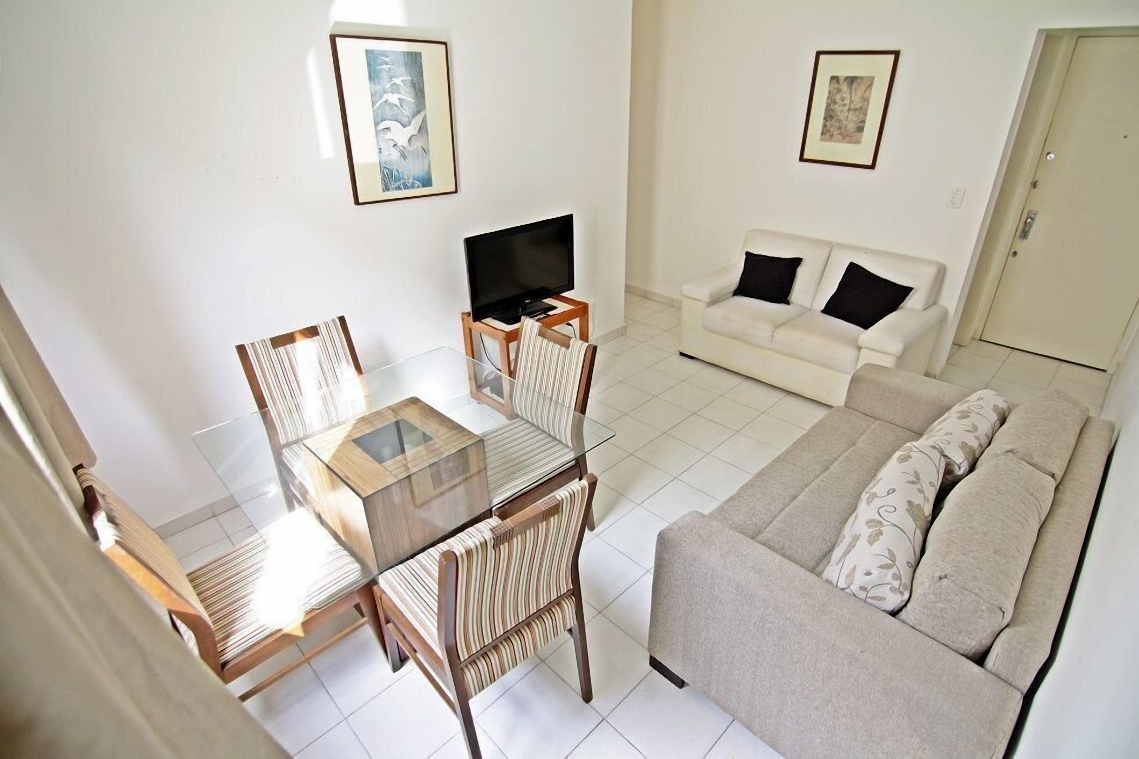 Uma sala de estar com sofá, televisão e mesa de jantar com cadeiras.