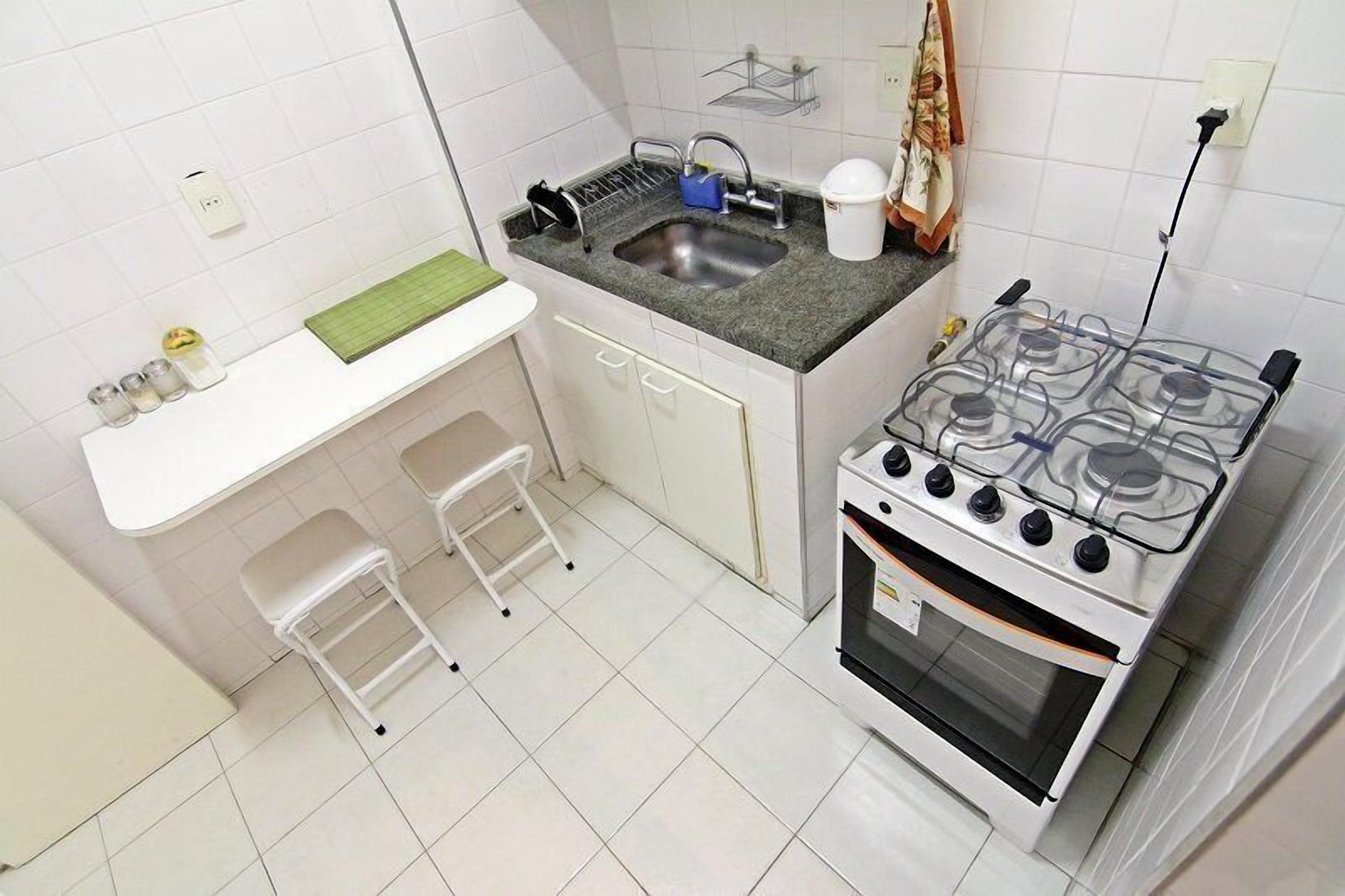 A compact kitchen with a gas stove, sink, and two stools.