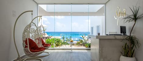 A modern room with a view of the ocean, a hanging chair, a small table, and a reception desk.