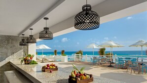 Un bar en un resort con vista al océano, asientos al aire libre y cestas de fruta.