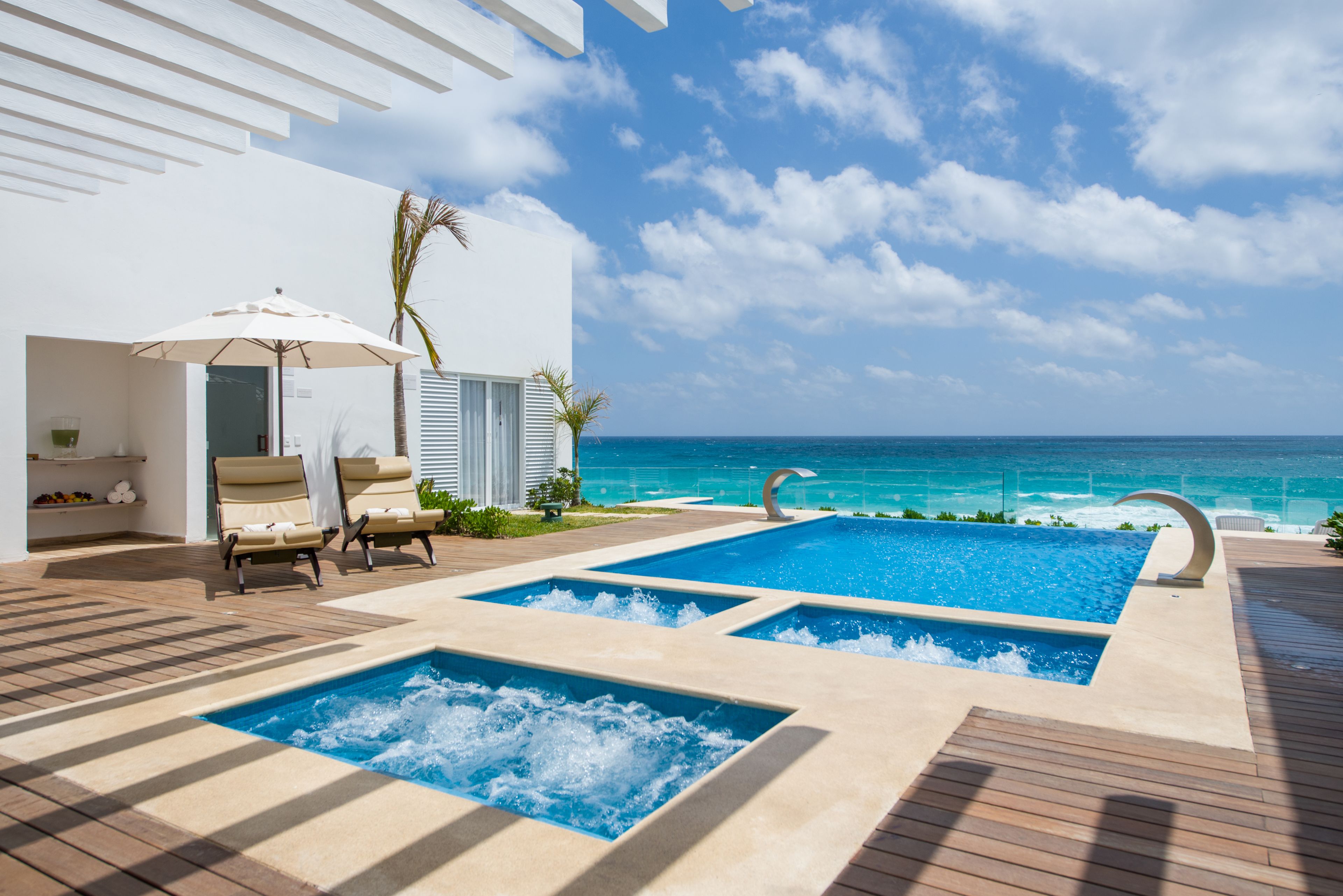 A pool area with two hot tubs, lounge chairs, and a view of the ocean.