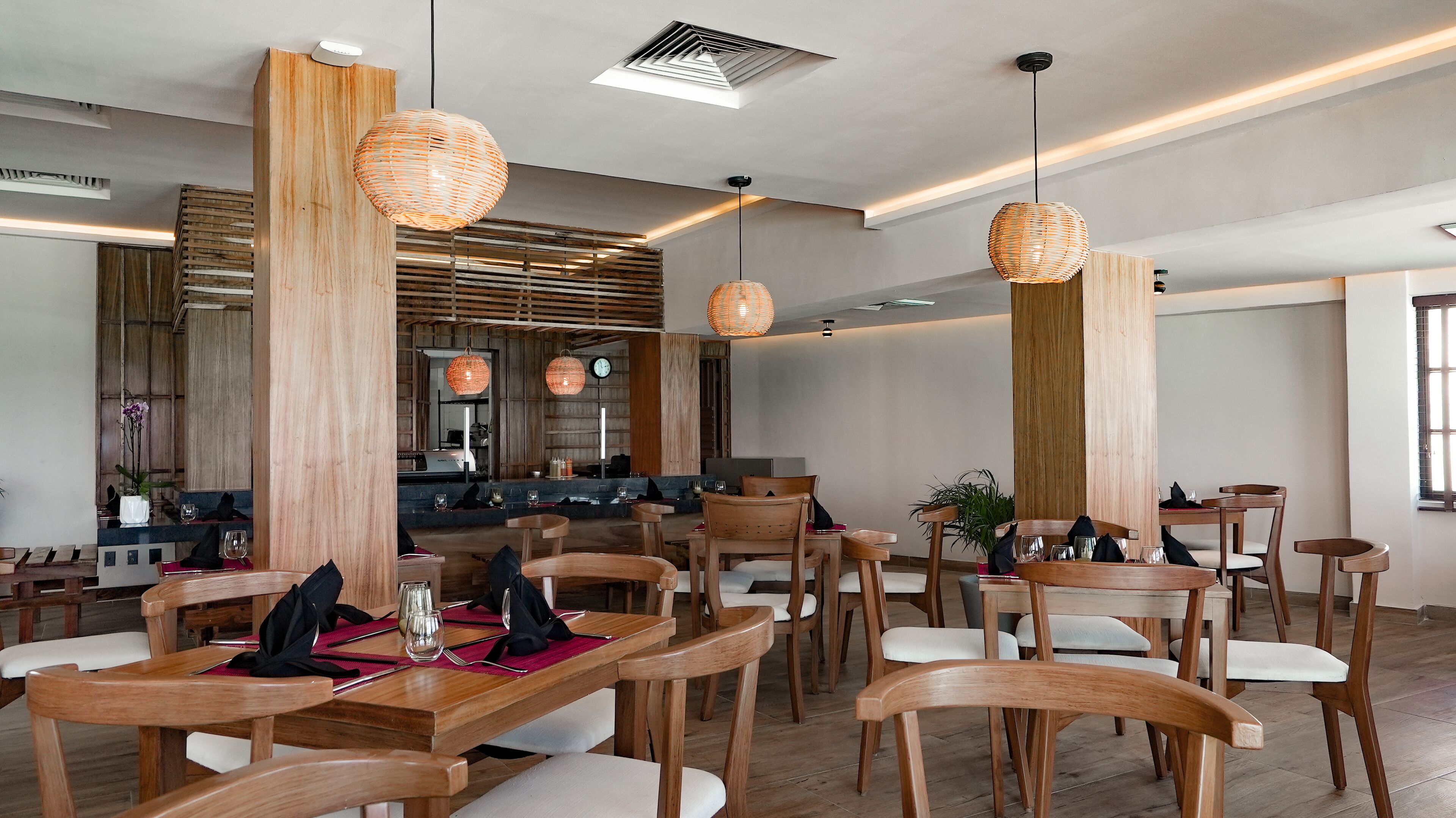 Un comedor moderno con muebles de madera, iluminación colgante y una barra visible al fondo.