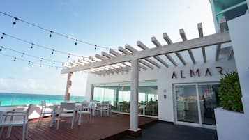 Restaurante com mesas ao ar livre e vista para o mar, uma pérgola com luzes e uma placa com o texto 'ALMAR'.