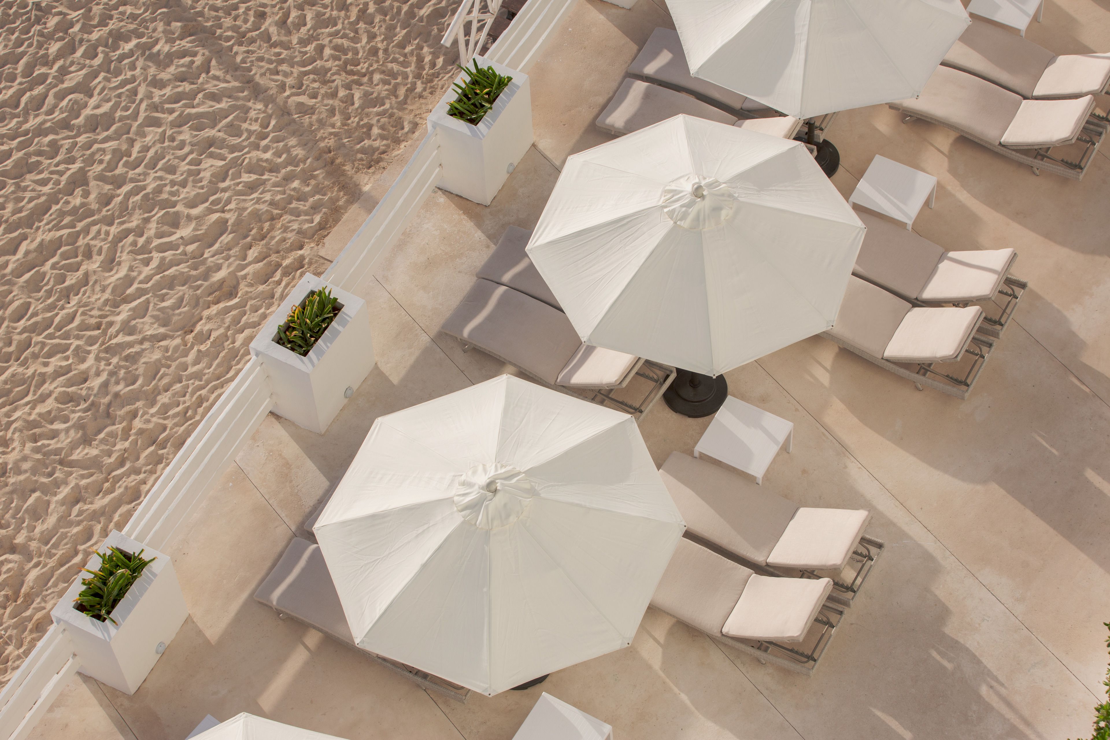 An outdoor seating area with white umbrellas and lounge chairs, adjacent to a sandy beach.