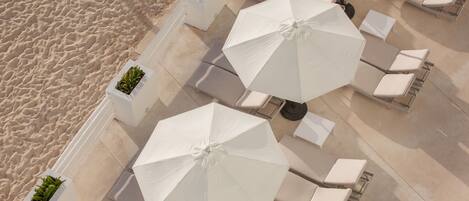 An outdoor seating area with white umbrellas and lounge chairs, adjacent to a sandy beach.
