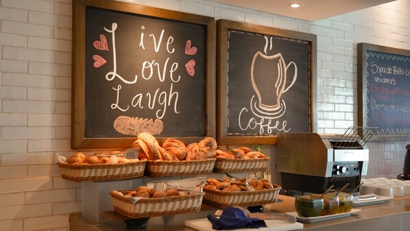 A breakfast buffet with bread and pastries, a coffee machine, and chalkboard signs with "Live Love Laugh" and "Coffee" messages. - Oleo Cancun Playa All Inclusive Resort (Cancun)