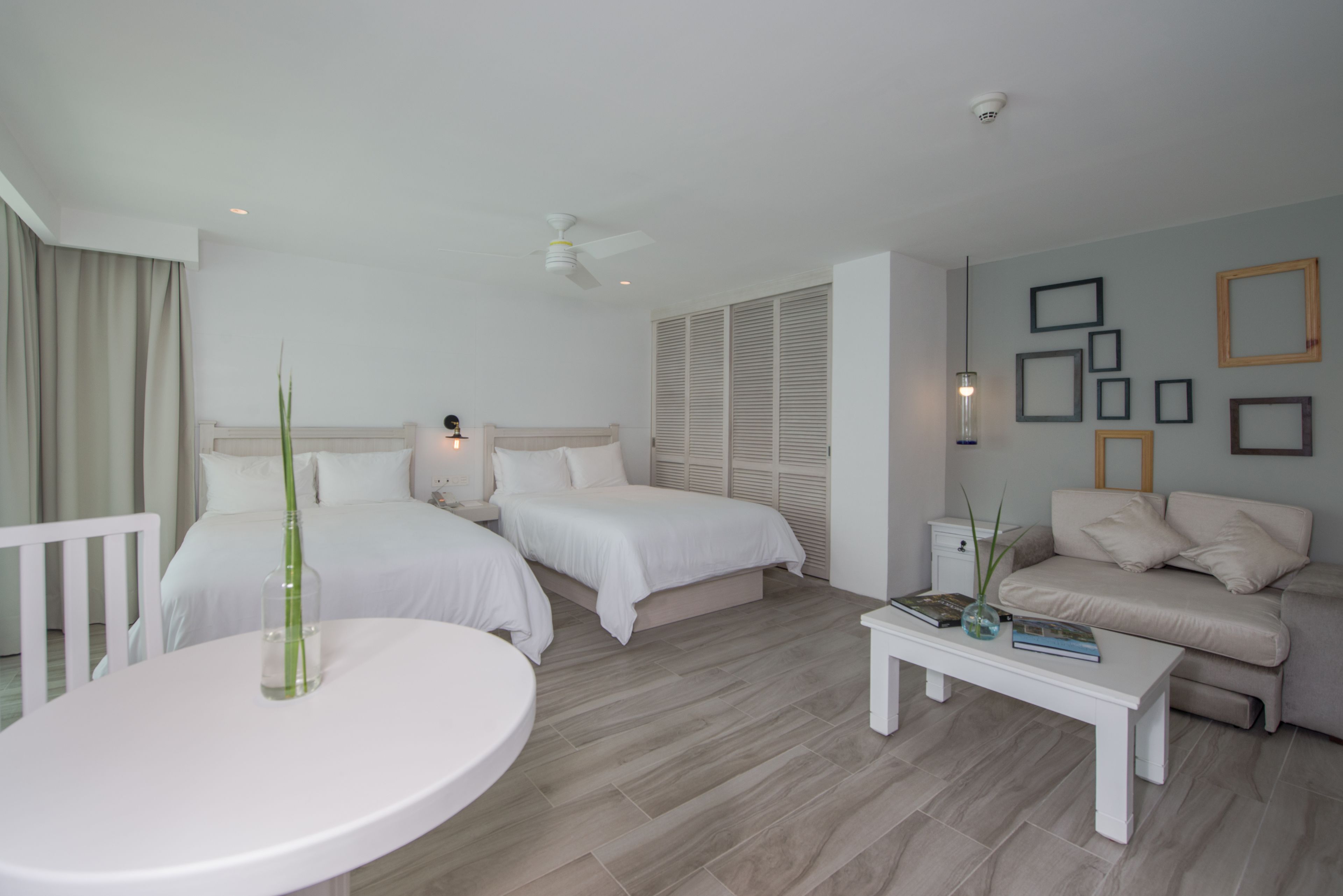 A modern hotel room with two beds, a round dining table, a sofa, and a ceiling fan.