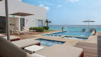 A pool area with lounge chairs and a view of the ocean.