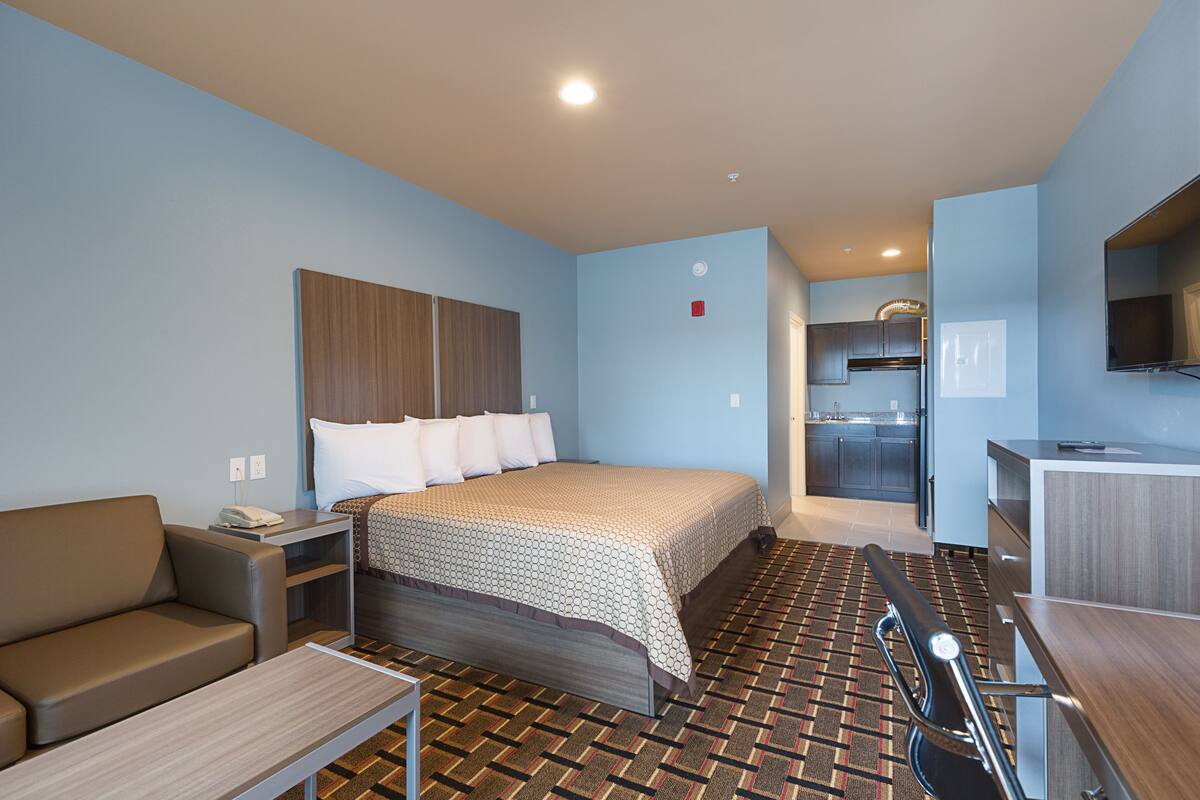 A hotel room with a bed, a sofa, a desk, a chair, and a kitchenette.