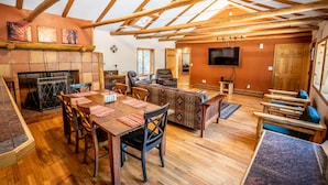A spacious living area with a wooden ceiling, a fireplace, a dining table with chairs, and a television mounted on the wall. - Colorado Bear Creek Cabins (Evergreen)