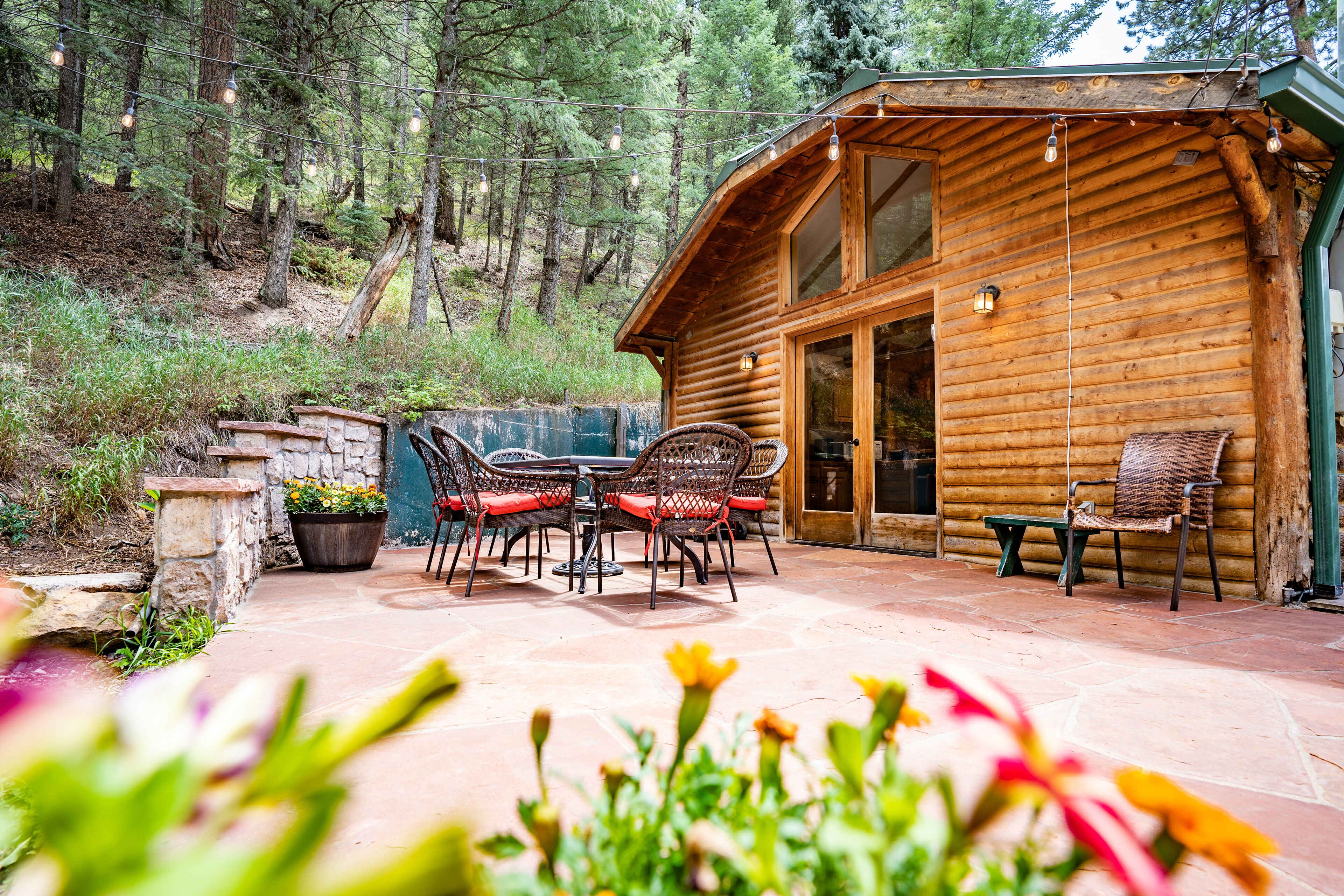 Una cabaña de madera con un patio, mobiliario exterior y un muro de piedra.
