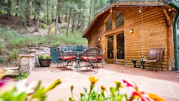 Una cabaña de madera con un patio, mobiliario exterior y un muro de piedra.