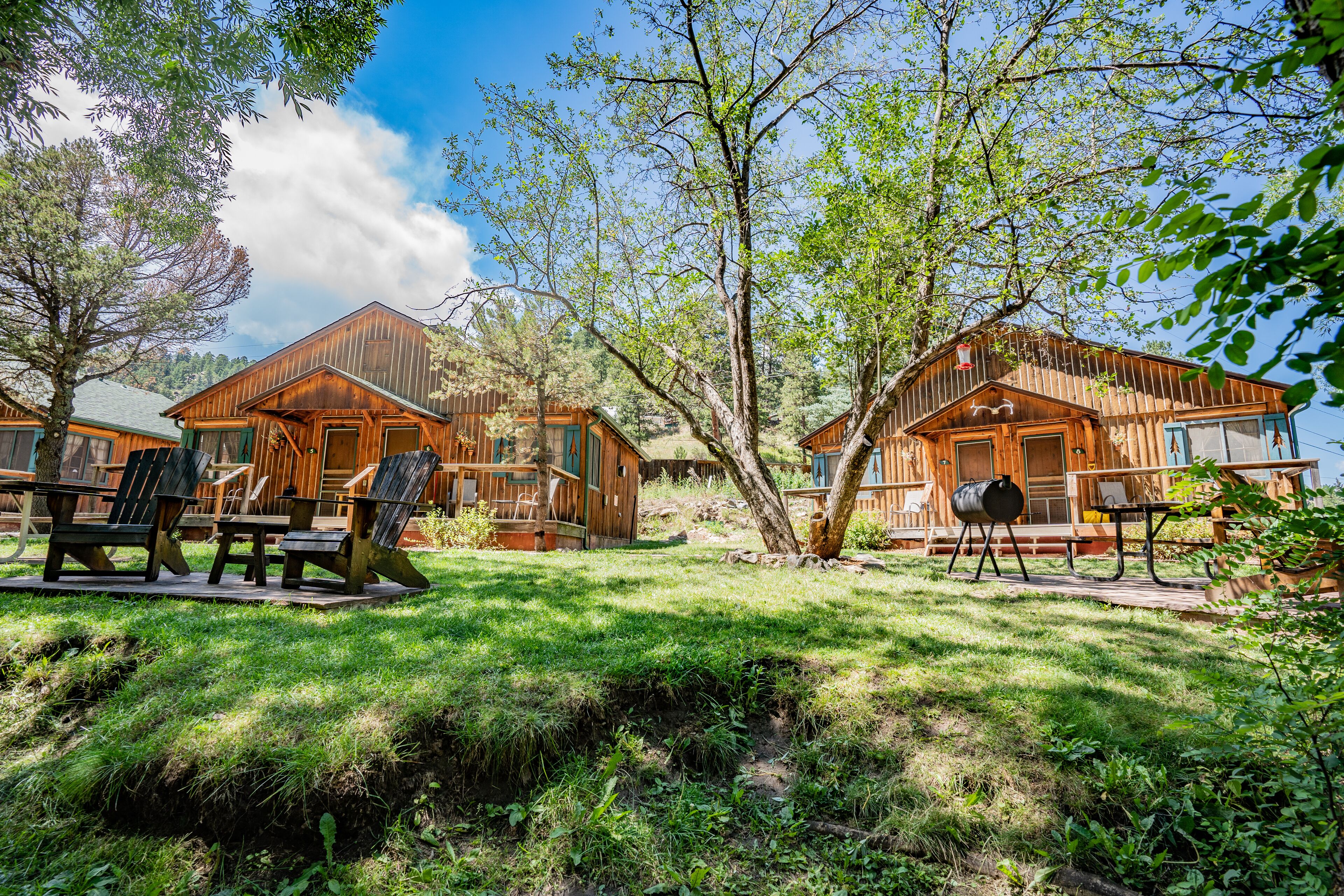 Alojamiento de estilo rústico tipo cabaña, con varias cabañas de madera, mobiliario exterior y un entorno natural.