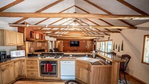 A spacious kitchen with wooden cabinets, a built-in microwave, a dishwasher, and a large island with a sink. - Colorado Bear Creek Cabins (Evergreen)