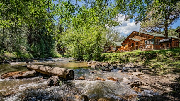 A wooden cabin by a flowing stream surrounded by dense forest. - Colorado Bear Creek Cabins (Evergreen)