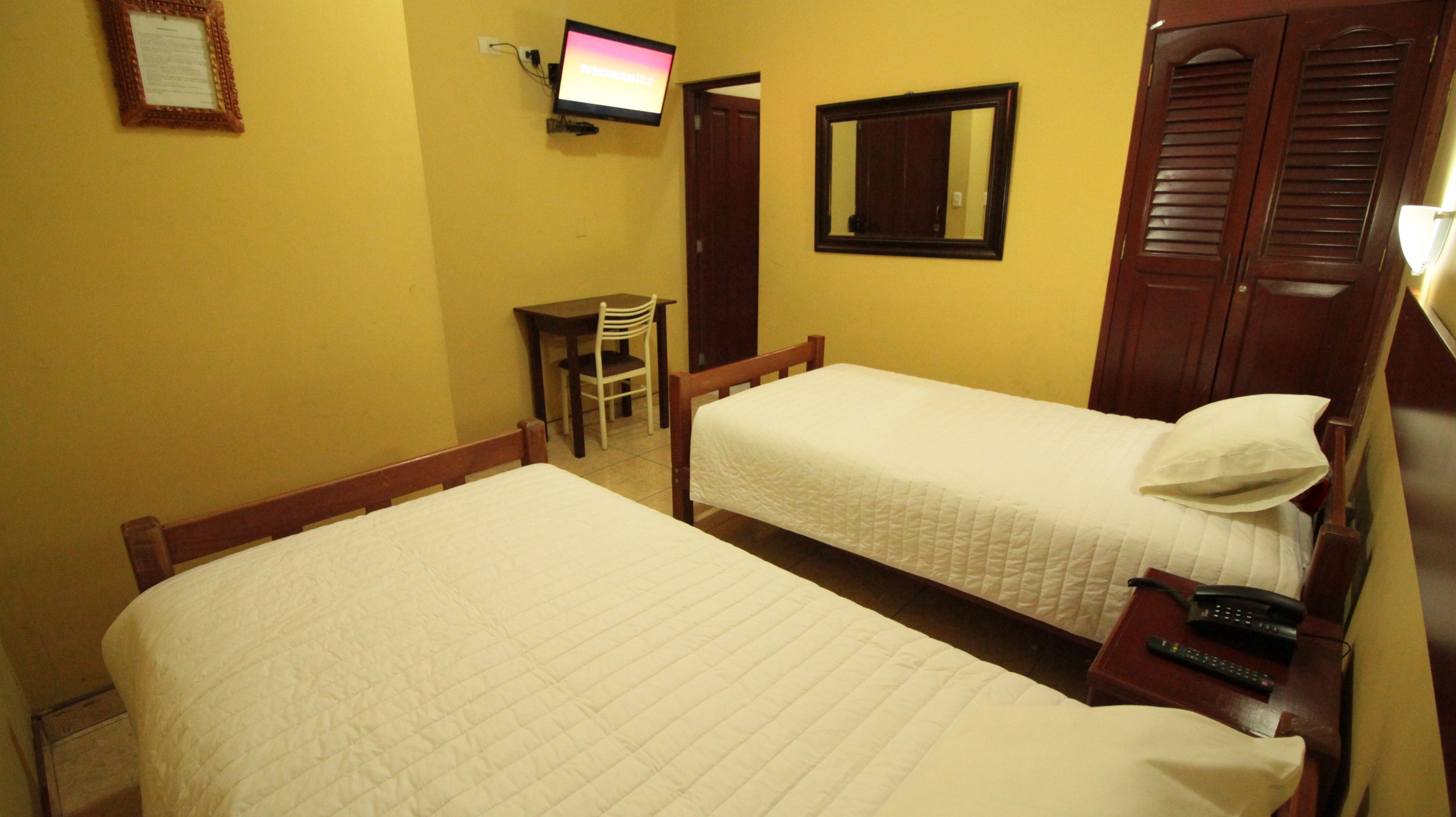 Una habitación de hotel con dos camas, un escritorio, una silla, un televisor y un espejo.
