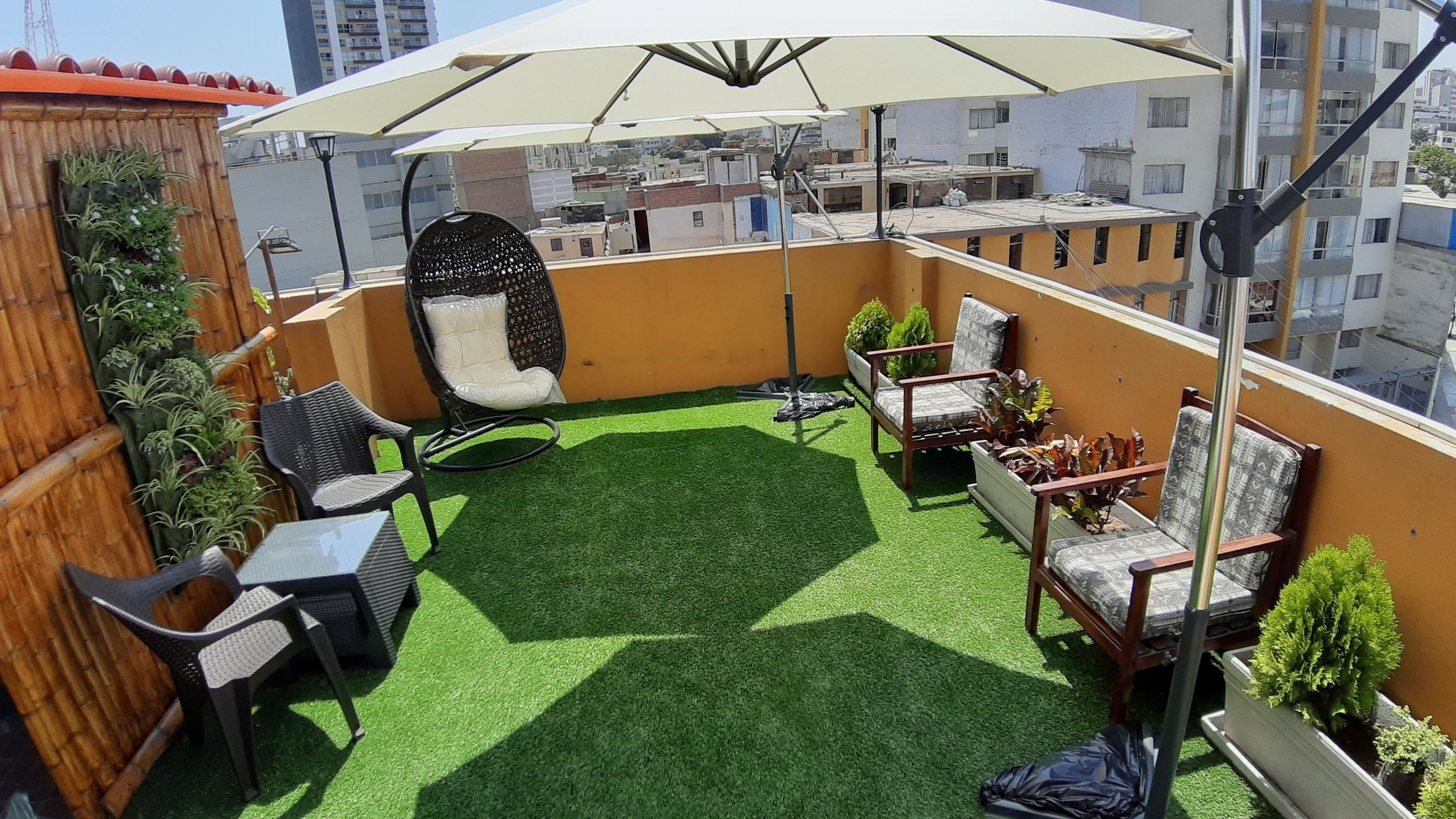 Una terraza en la azotea con césped artificial, mobiliario de exterior y un amplio paraguas.