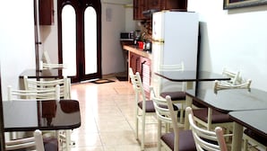 A dining area with white chairs and dark tables, a white refrigerator, and wooden cabinets in the background. - Pretty House Hostel (Lima)