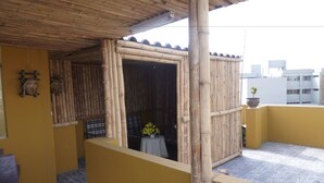 A bamboo structure with a small table and potted plant, a yellow wall, and a tiled floor. - Pretty House Hostel (Lima)