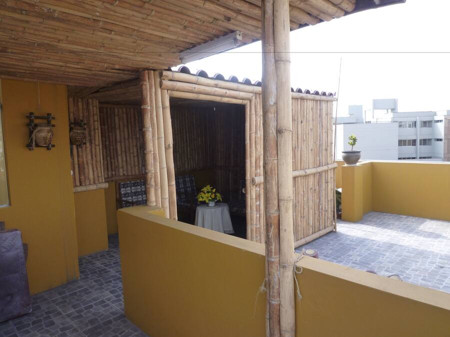 Estructura de bambú con una pequeña mesa y una planta en maceta, una pared amarilla y un suelo de baldosas.