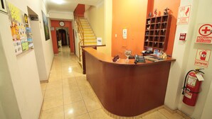 A hotel reception area with a curved desk, a clock, a fire extinguisher, and a staircase leading to another floor. - Pretty House Hostel (Lima)