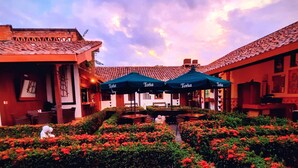 A courtyard with red flowers, outdoor seating, and a building with a tiled roof. - Hotel La Posada del Doctor (León)