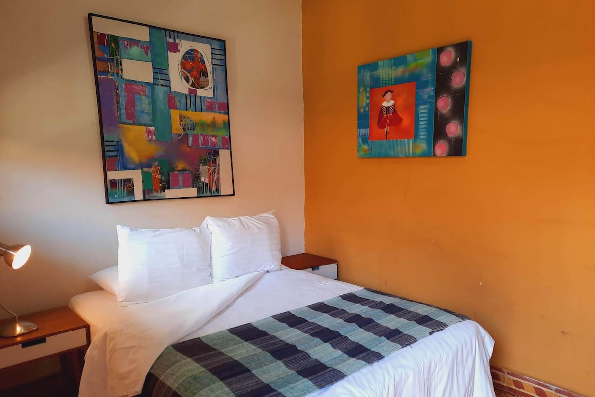 Una habitación de hotel con una cama, una mesita de noche, una lámpara y dos cuadros en las paredes.