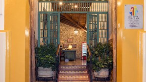 A yellow-walled entrance with a wooden door, a staircase, and a sign reading "Ruta Colonial y de los Volcanes." - Hotel La Posada del Doctor (León)