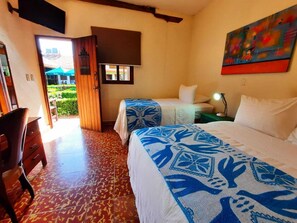A hotel room with two beds, a desk, a chair, and a view of the garden through an open door. - Hotel La Posada del Doctor (León)