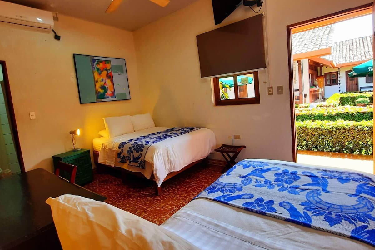 Un dormitorio con dos camas, un ventilador de techo, un televisor montado en la pared y una ventana con vistas al exterior.