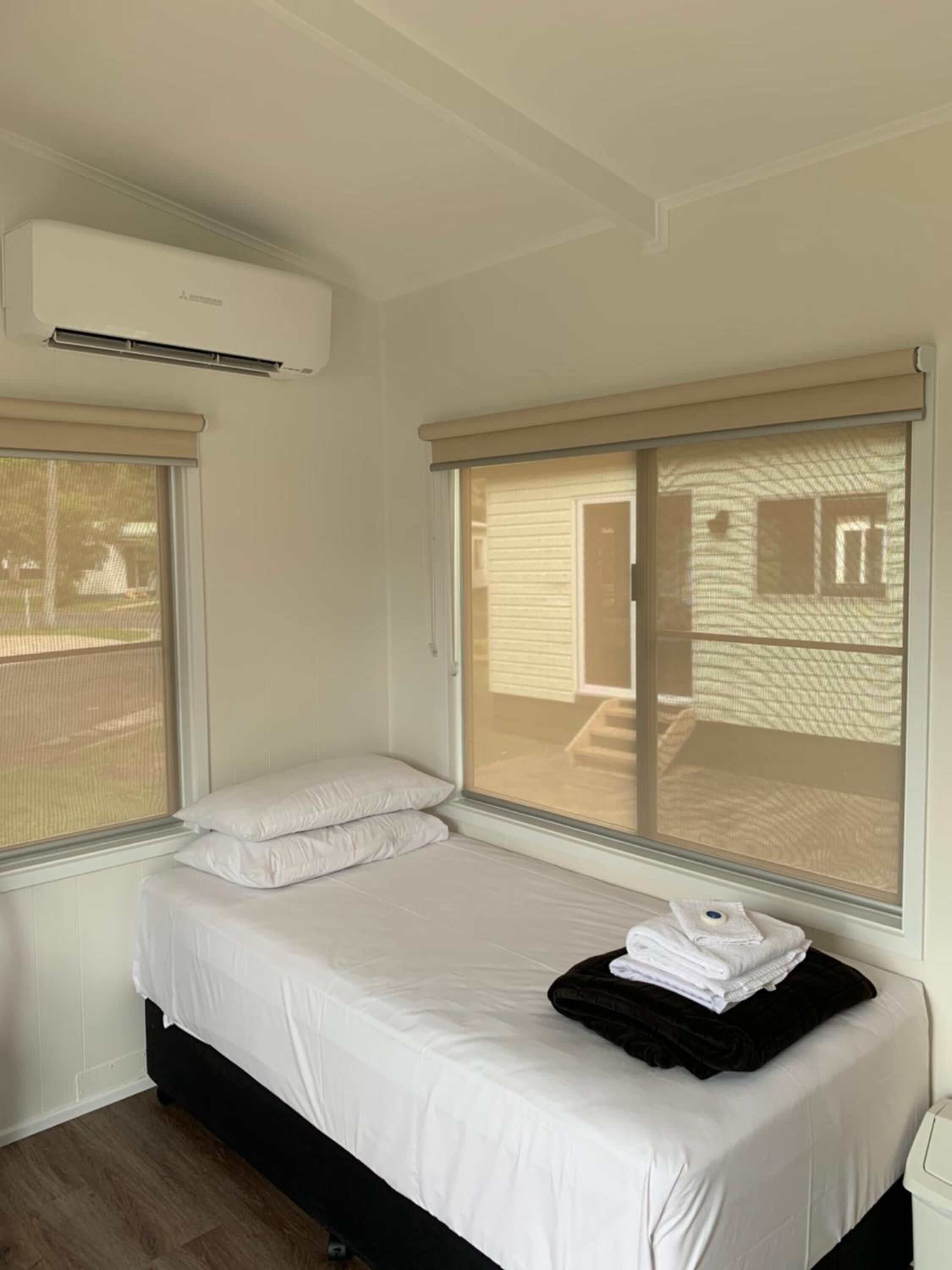 Una cama individual con ropa de cama blanca, cabecera negra y ventana con vista a un edificio.