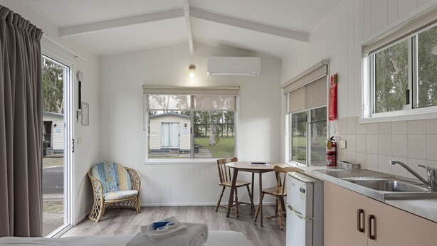 A compact room with a bed, a dining table with chairs, a kitchenette, and a window overlooking a small outdoor area.