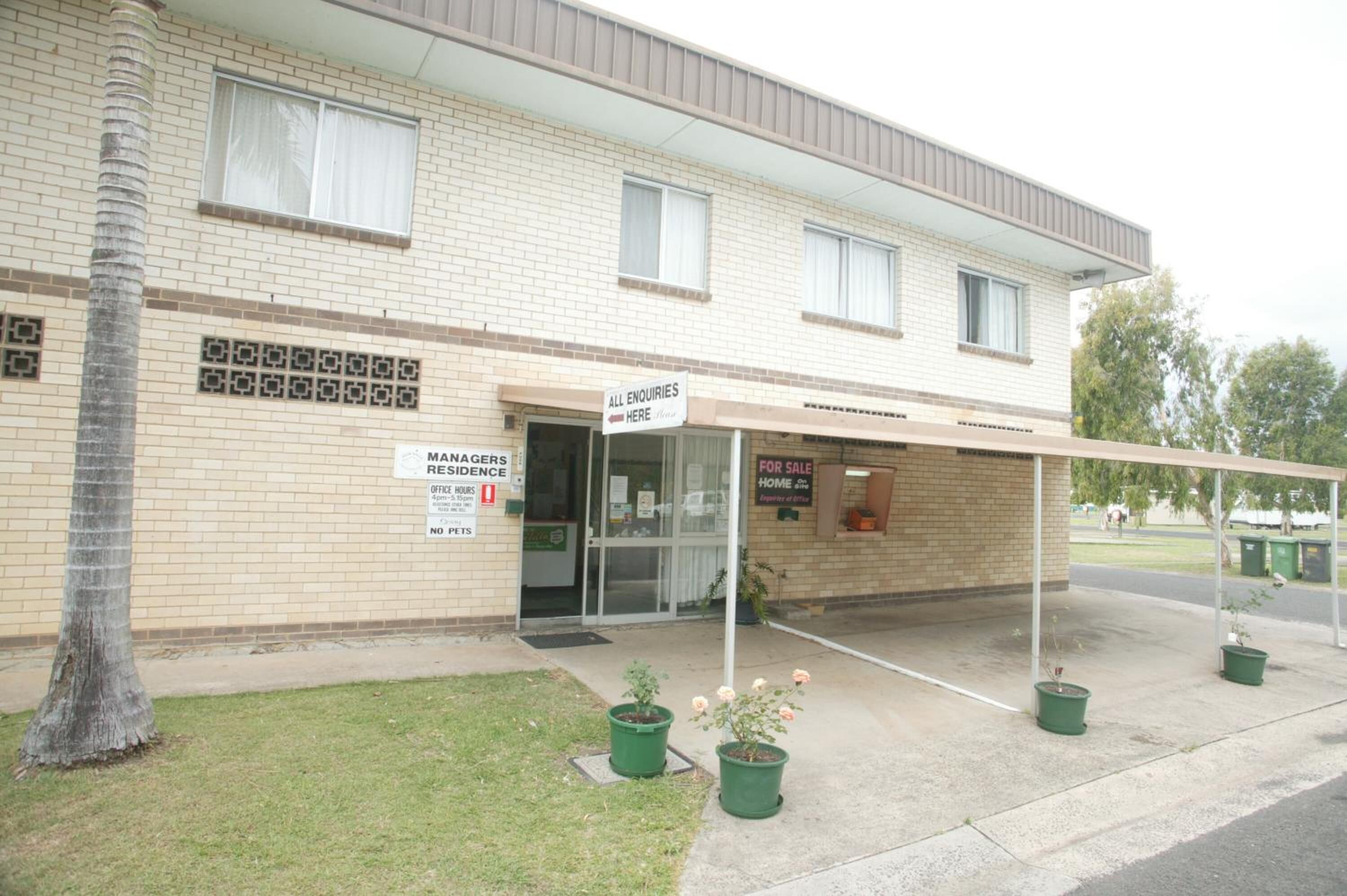 A two-story building with a sign indicating it's for sale. There are potted plants in front and a covered area with a sign for enquiries.
