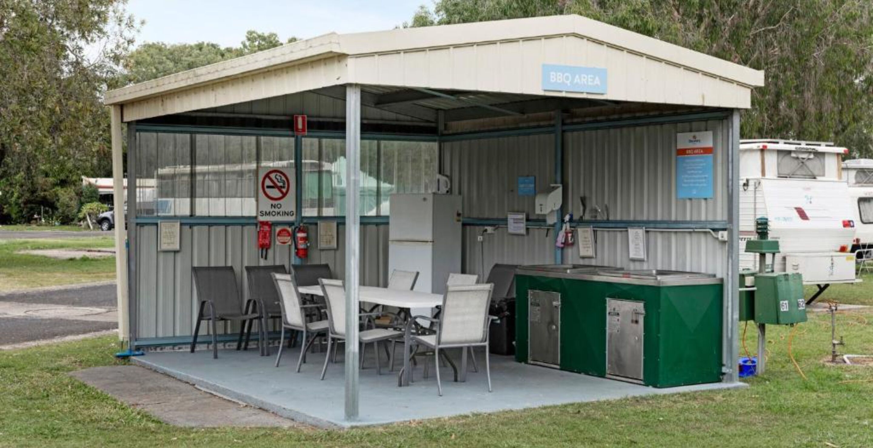 A covered outdoor area with a BBQ station, seating, and a no smoking sign.