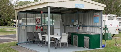 Un espacio al aire libre cubierto con una estación de barbacoa, asientos y un letrero de prohibición de fumar.